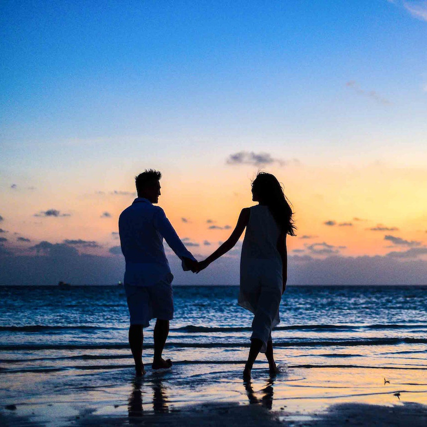 A couple walking on the beach near the shore during sunset